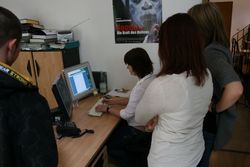 Drei Schüler sehen einer Bediensteten bei der Arbeit am Bildschirm zu