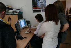 Drei Schüler sehen einer Bediensteten bei der Arbeit am Bildschirm zu Drei Schüler sehen einer Bediensteten bei der Arbeit am Bildschirm zu